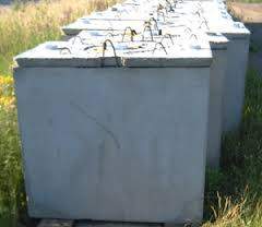 A row of large, grey concrete blocks with metal loops on top arranged on the grass near a path.